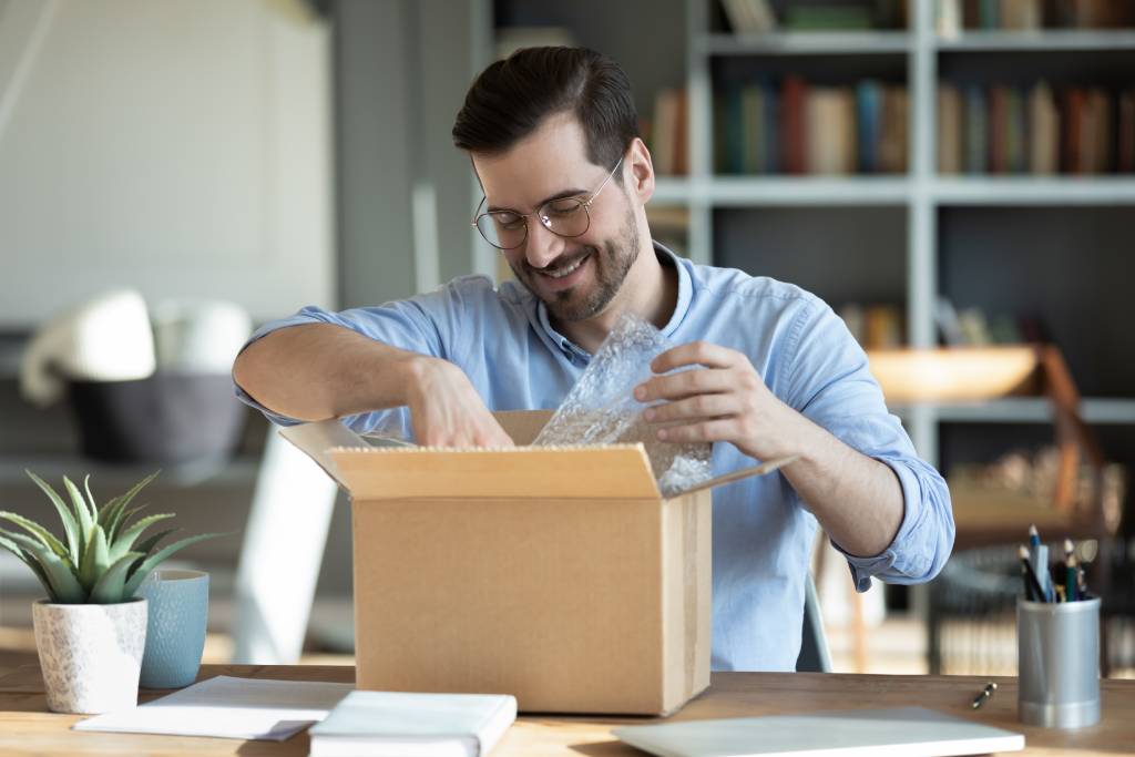 A man in glasses opens a box at his desk.